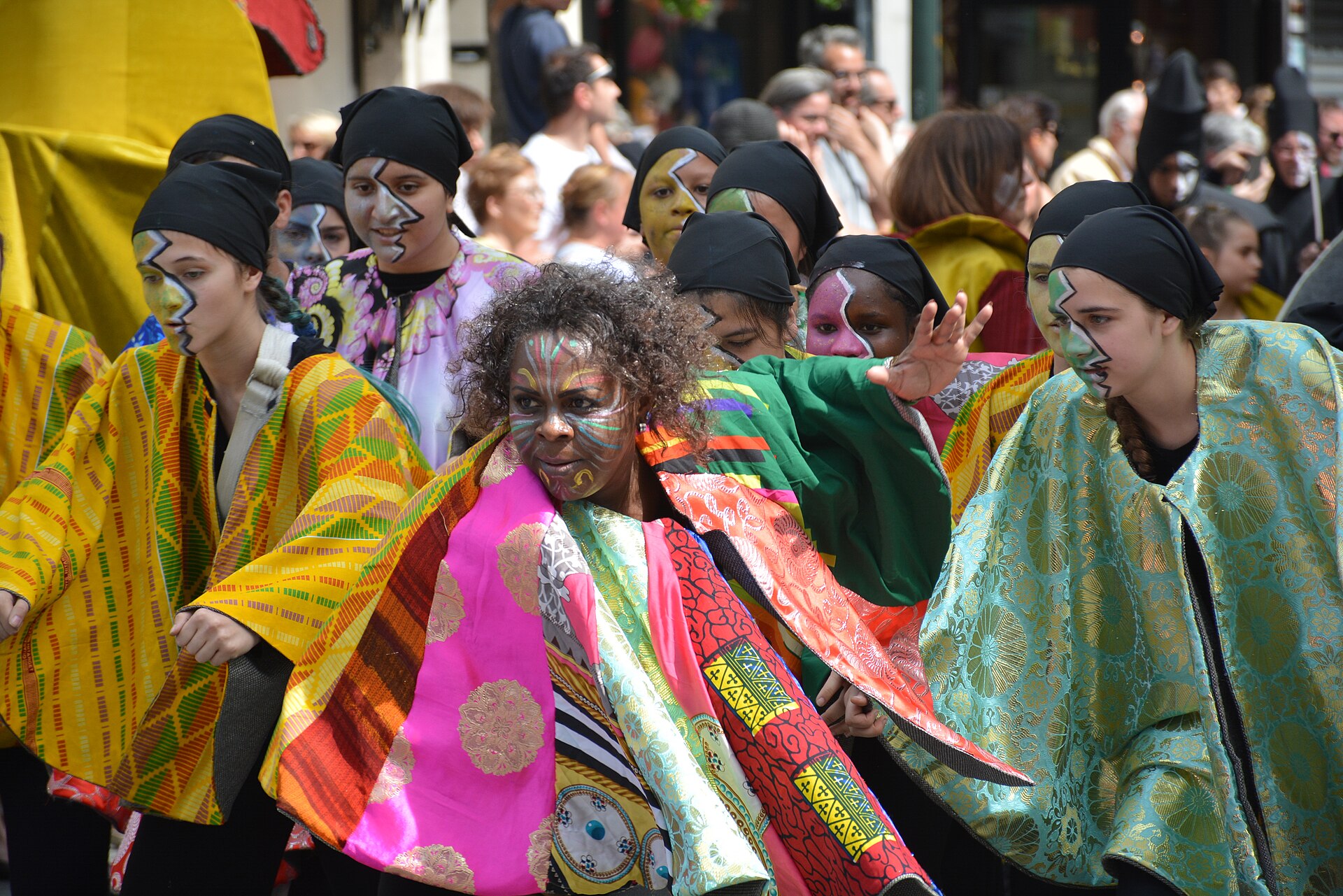 Group wearing colorful costumes and face paint performing at a lively outdoor parade.