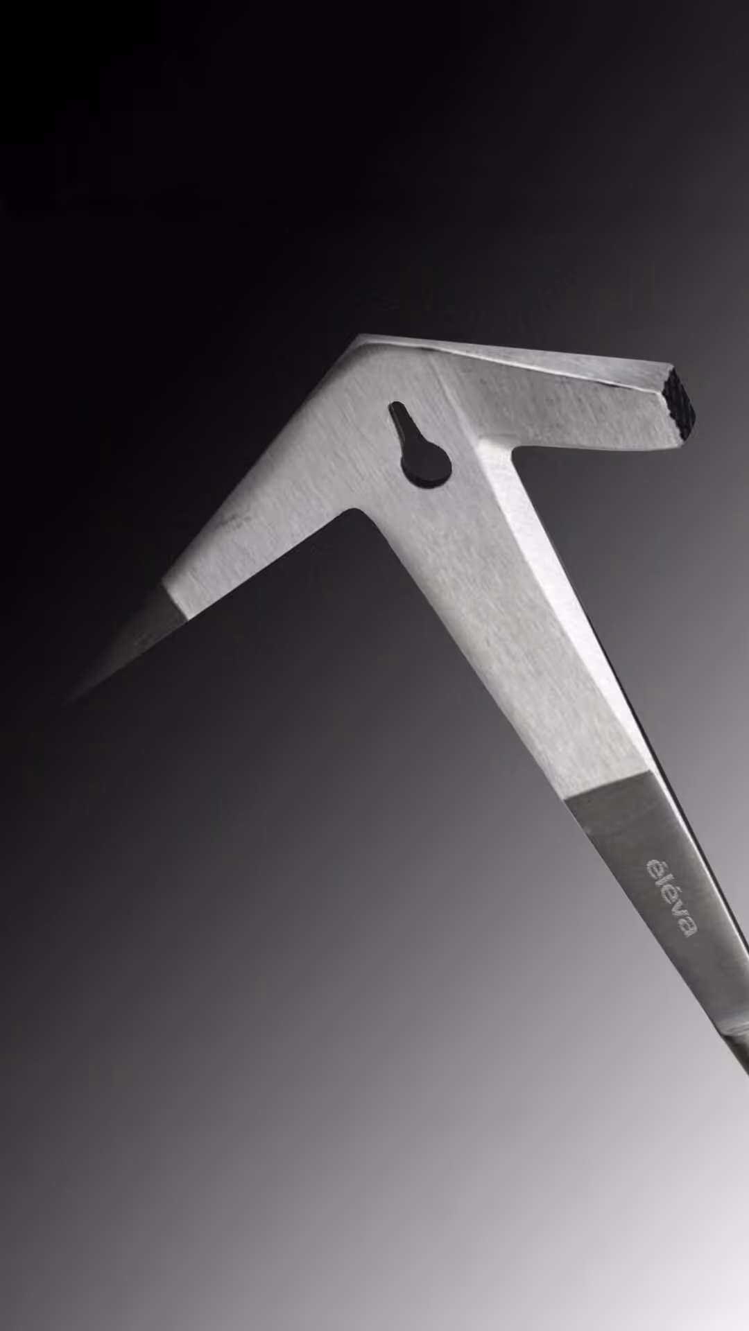 Metal tool with sharp pointed ends and a cutout hole against a gradient black to white background.
